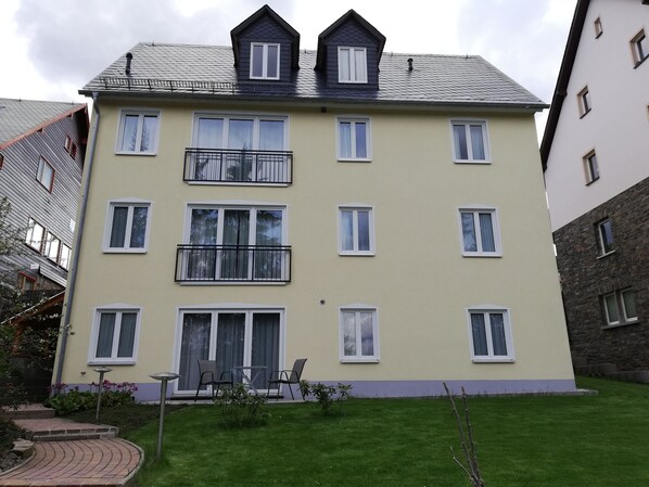 A multi-story residential building with a flat roof, multiple balconies, and a well-maintained lawn.