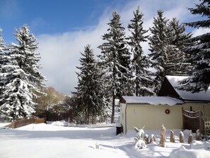 A snow-covered landscape with tall evergreen trees, a small building with a sloped roof, and a wooden fence. - Appartementhaus Hollandhaus (Oberwiesenthal)
