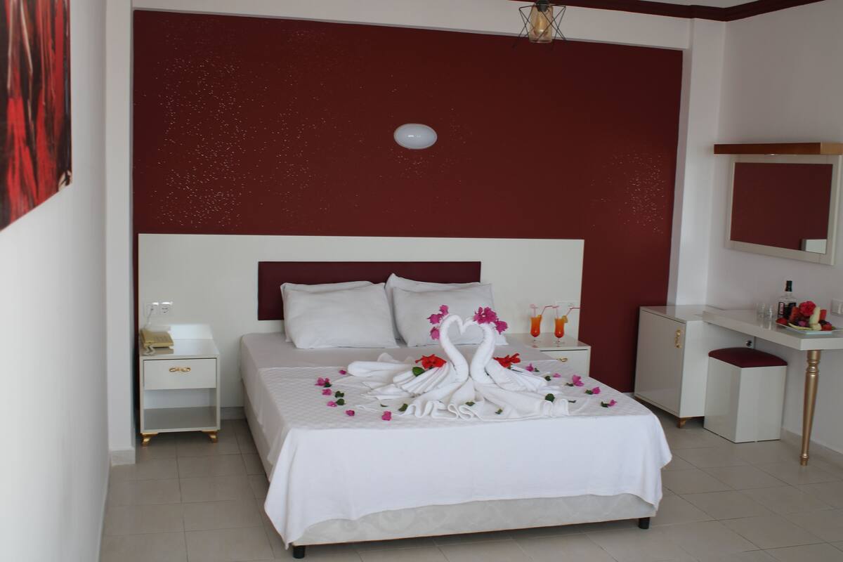 A neatly arranged hotel room with a large bed, a bedside table, a small desk, and a mirror.