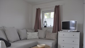 A modern living room with a grey sofa, a white dresser, a wooden coffee table, and a television on a stand. - Romantic quiet chalet with a beautiful garden (Algolsheim)