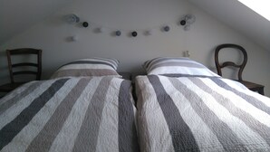 A bedroom with two beds, striped bedding, a string of decorative balls on the ceiling, and wooden furniture. - Romantic quiet chalet with a beautiful garden (Algolsheim)