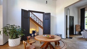 A dining area with a round wooden table and chairs, a potted plant, and a staircase with a railing. - Kind of OJ (Bruges)