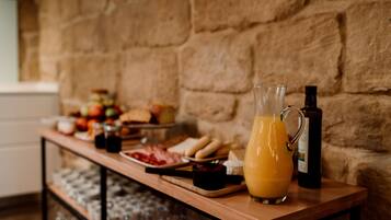 Un bufé de desayuno con diversas comidas y una jarra de jugo de naranja sobre una mesa de madera frente a una pared de piedra.