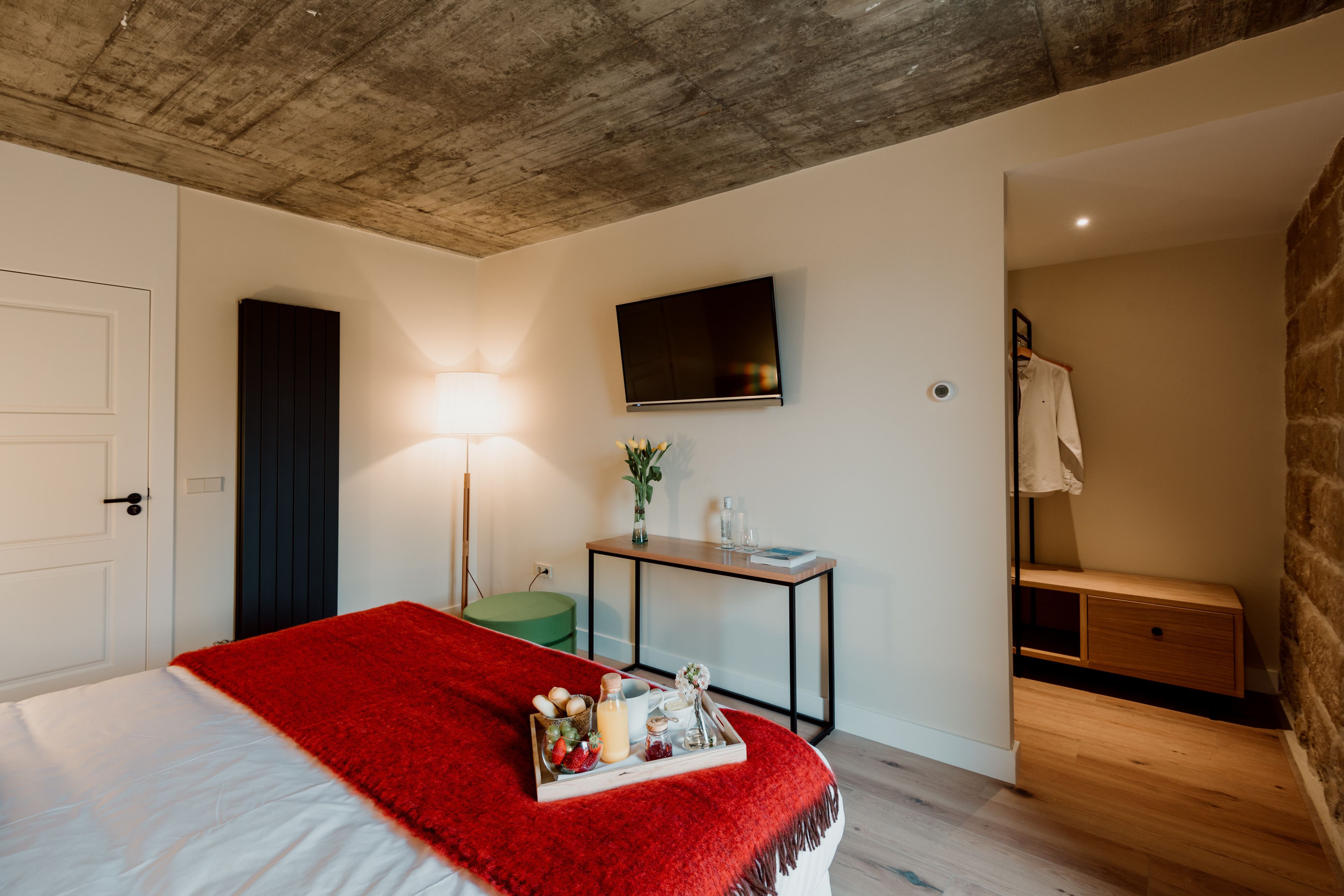 Ein Schlafzimmer mit Bett, Nachttisch mit Lampe, Fernseher an der Wand und einer Holzbank.