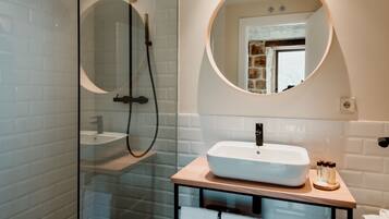 Un baño moderno con ducha envuelta en vidrio, un espejo redondo, un lavabo blanco y baldosas de suelo estampadas.