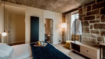 A modern bedroom with a stone wall, a wooden ceiling, a bed with a blue rug, a bedside table, and a hanging light fixture.