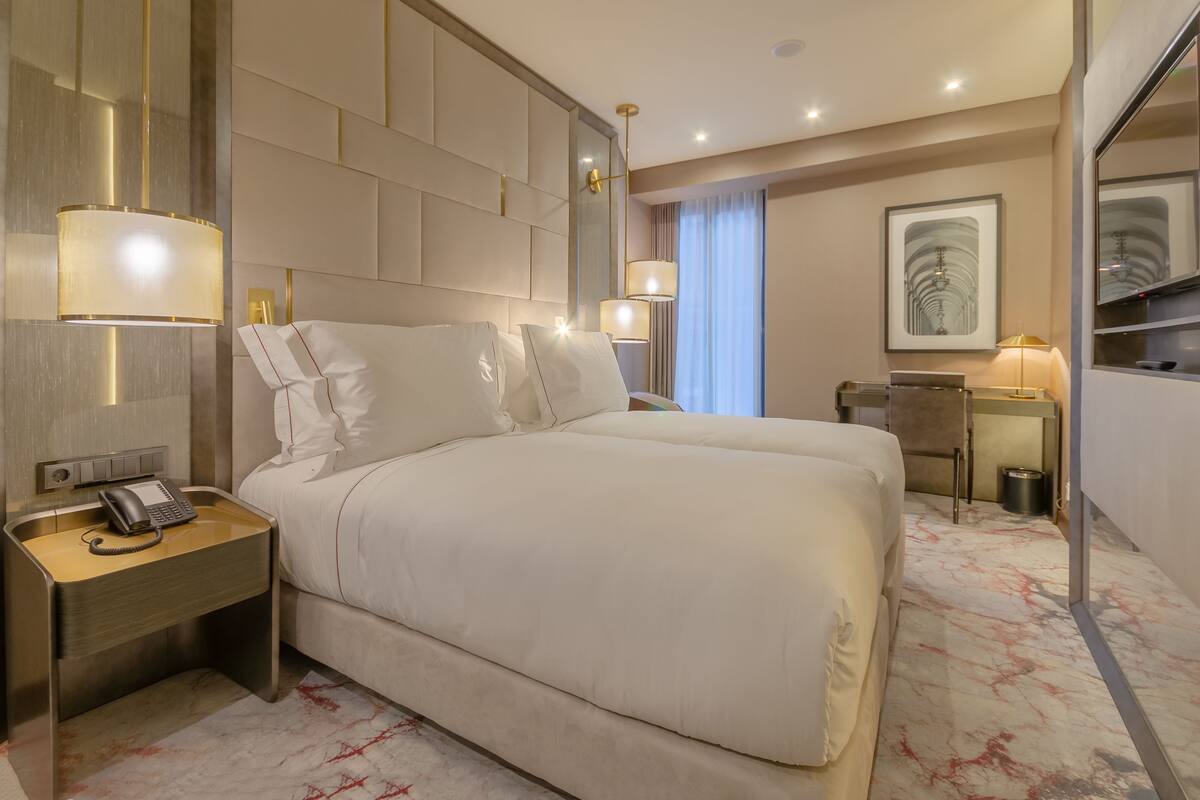 A hotel room with a large bed, bedside lamps, a desk, and a mirror.