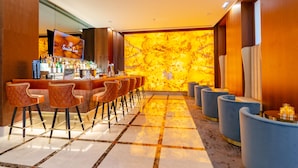 Una zona de bar con una barra alargada, varios taburetes y una pared grande iluminada.