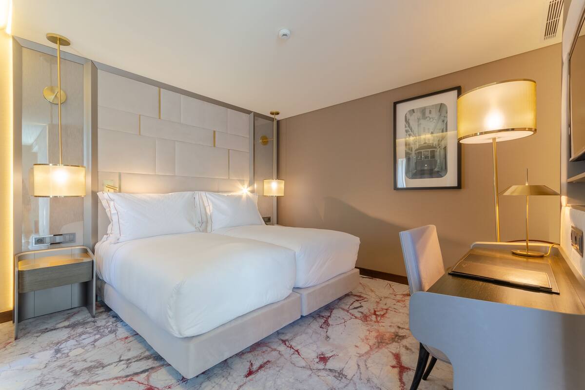 A modern hotel room with a large bed, bedside tables, a desk, and a chair.