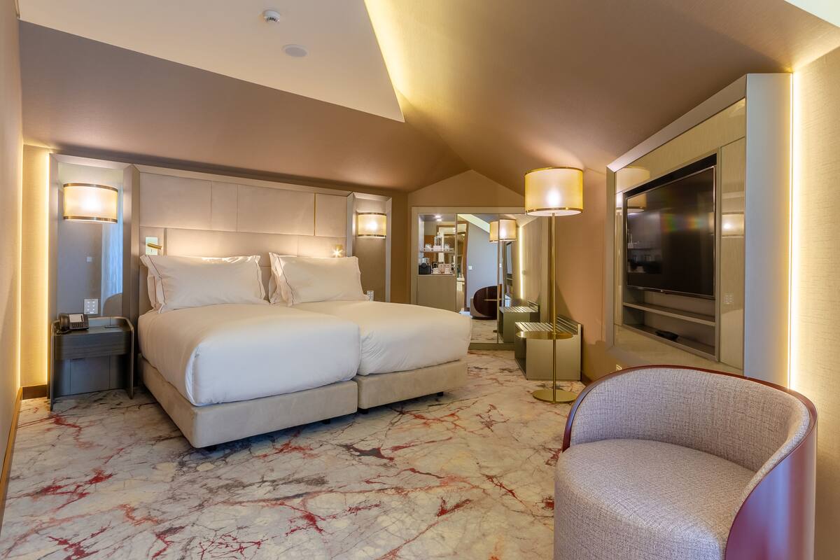 A modern hotel room with a large bed, bedside tables, a TV, and a seating area.