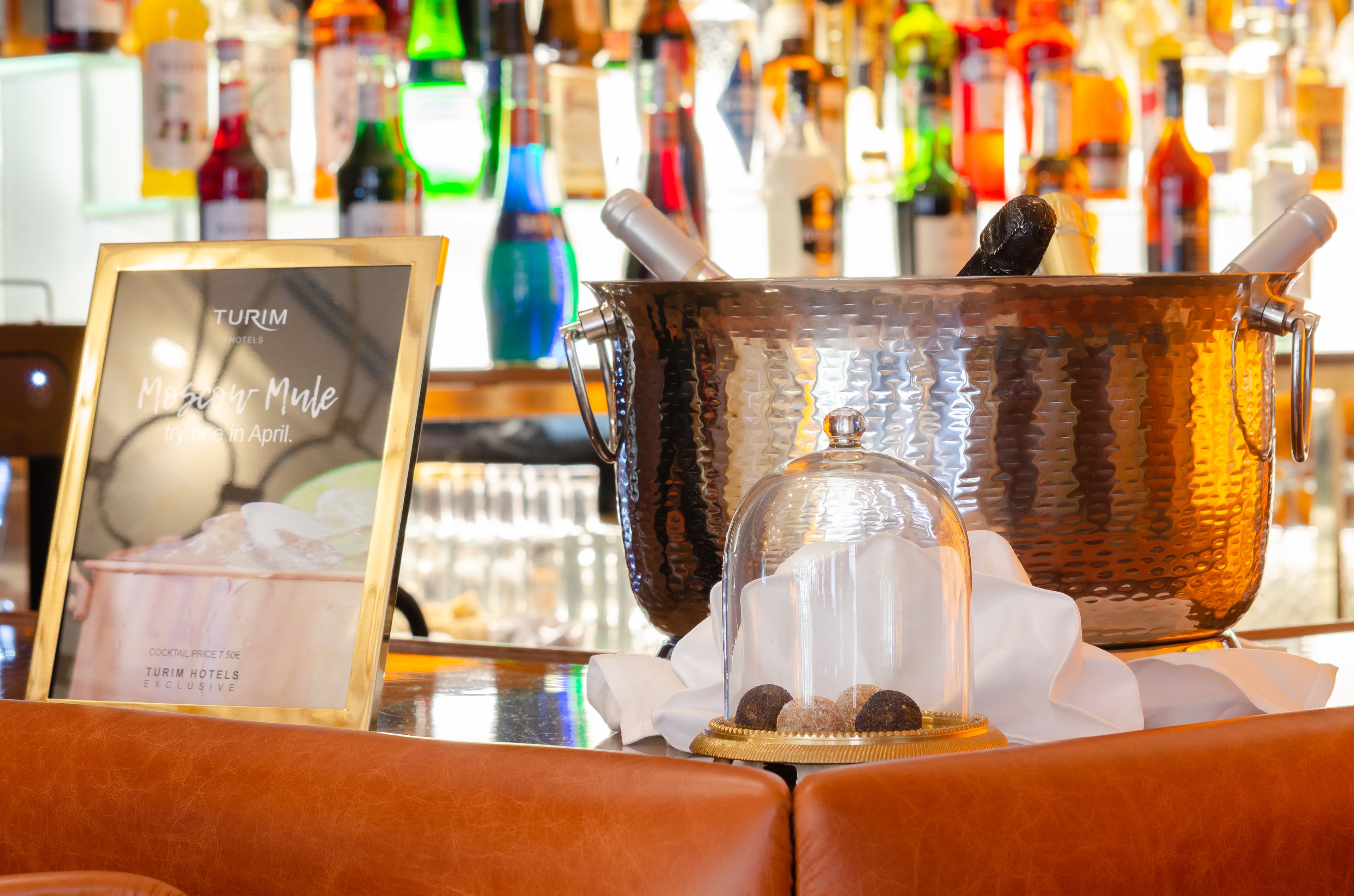 Zona de bar con un cartel enmarcado que dice 'Turim Hotels Moscow Mule' y una olla de cobre con asa.