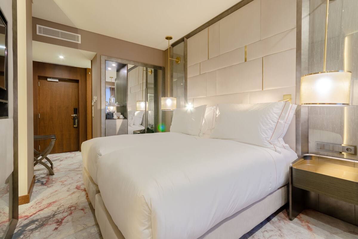 A hotel room with a large bed, a bedside table with a lamp, a mirror, and a chair.