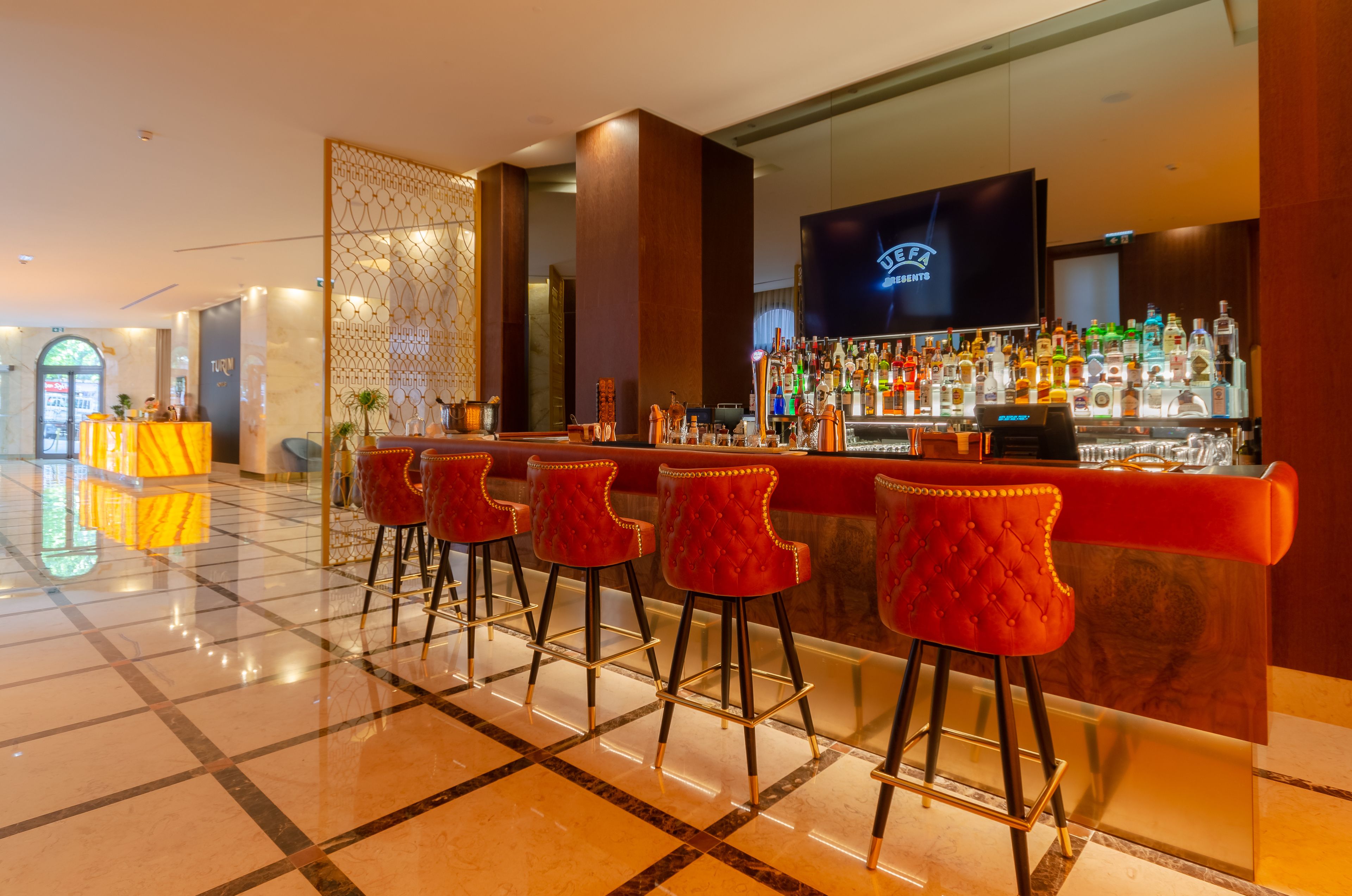 Un espace bar doté d’un sol en marbre poli, de tabourets de bar rouges et d’un présentoir bien garni de bouteilles d’alcool.