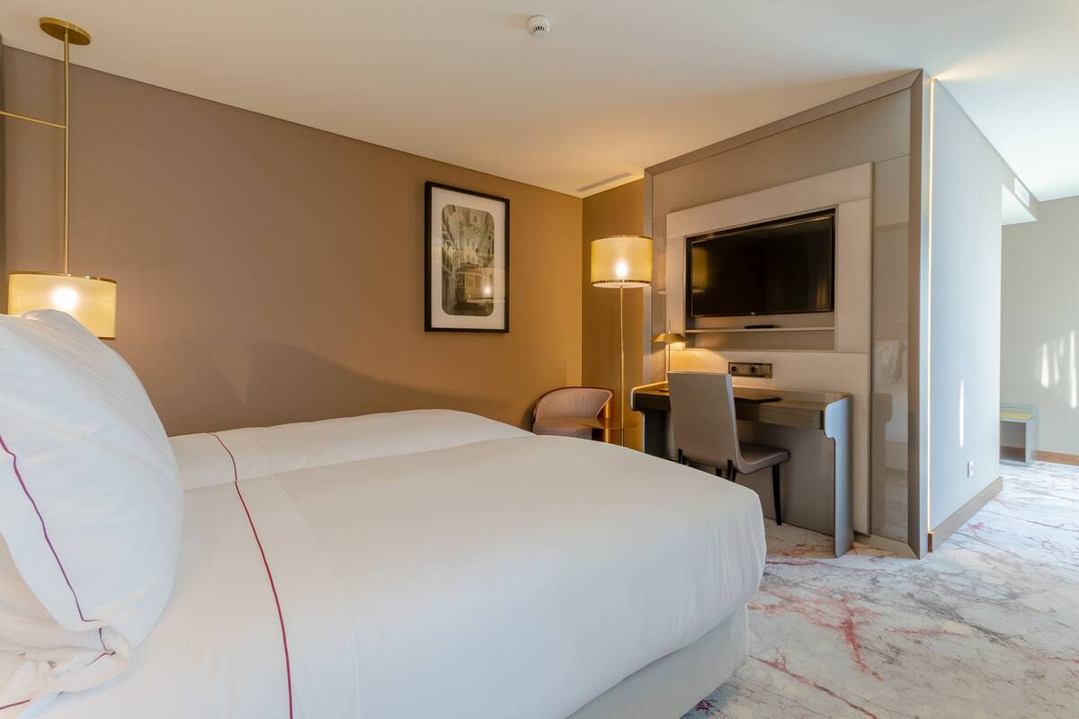 A hotel room with a large bed, a desk, a chair, a TV, and a framed picture on the wall.