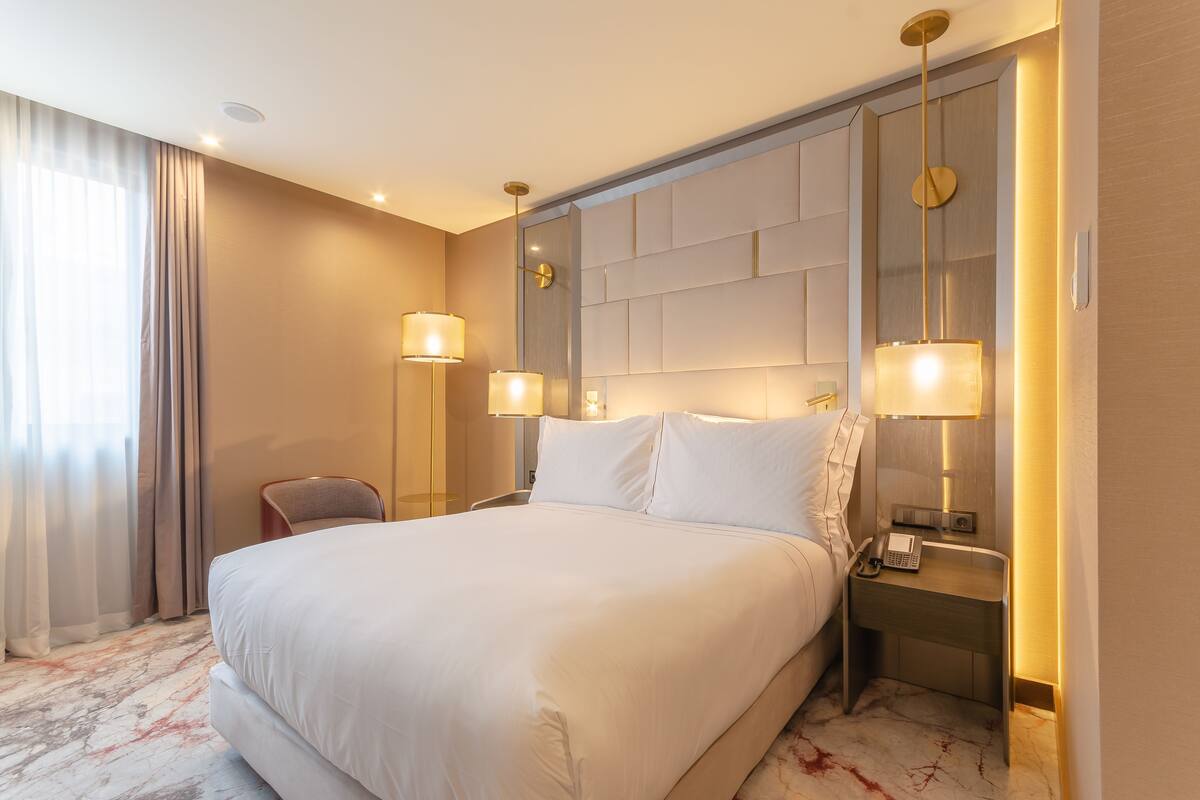 A hotel room with a large bed, two bedside tables with lamps, a chair, and a marble-patterned floor.