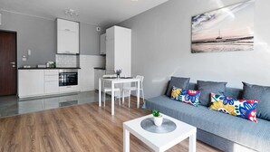 A modern living room with a grey sofa, colorful pillows, a white coffee table, and a painting of a sunset over water. - Warszawa-Wlochy Brilliant Apartment (Warsaw)