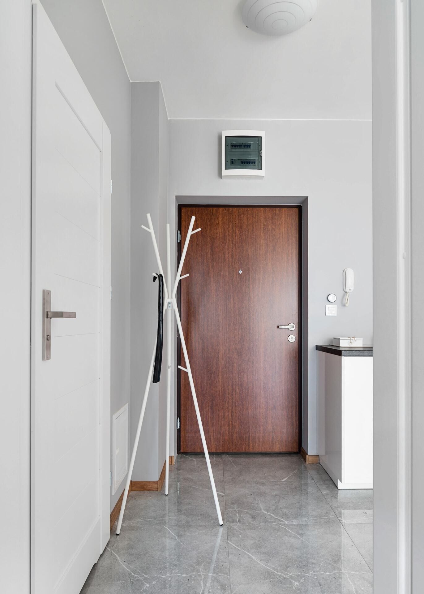 Ein Flur mit einer Holztür, einem Kleiderständer, einem weißen Schrank und einer Deckenleuchte.