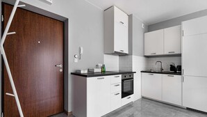 A modern kitchen with white cabinets, a black countertop, and a wooden door. - Warszawa-Wlochy Brilliant Apartment (Warsaw)