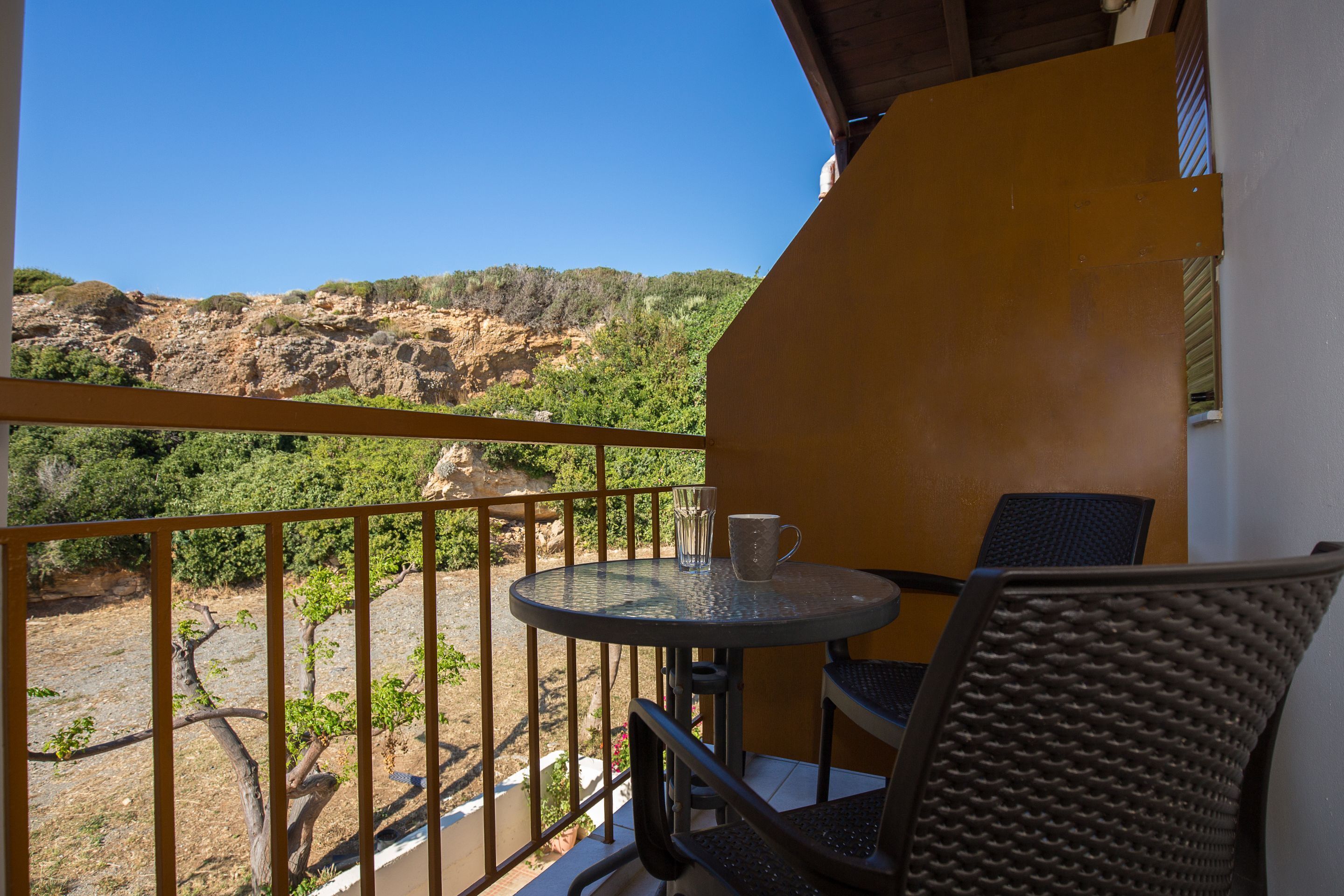 Un balcón con mesa y sillas, con vistas a un paisaje rocoso con vegetación.