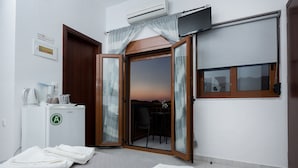 A hotel room with a sliding glass door leading to a balcony, a small kitchenette, and a view of the sunset. - En Plo Rooms (Kissamos)
