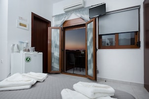 A hotel room with a sliding glass door leading to a balcony, a small kitchenette, and a view of the sunset.