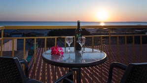 A table with a bottle and two glasses on a balcony overlooking the ocean at sunset. - En Plo Rooms (Kissamos)