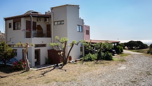 A two-story building with a balcony, a gravel driveway, and a view of the sea. - En Plo Rooms (Kissamos)