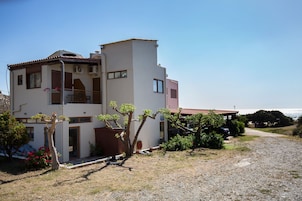 A two-story building with a balcony, a gravel driveway, and a view of the sea.