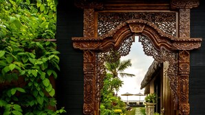 An ornate wooden archway leading to a pathway with a thatched-roof structure in the background. - Villa Sakina (Nosy Be)