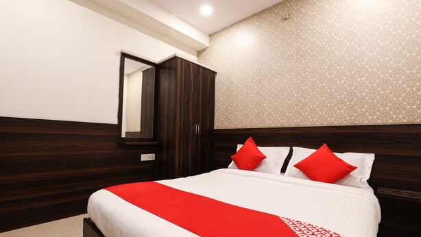 A neatly made bed with a red and white bedspread, a wooden wardrobe, and a mirror on the wall. - OYO 14194 Hotel Deccan Lodging and Boarding (Hyderabad)