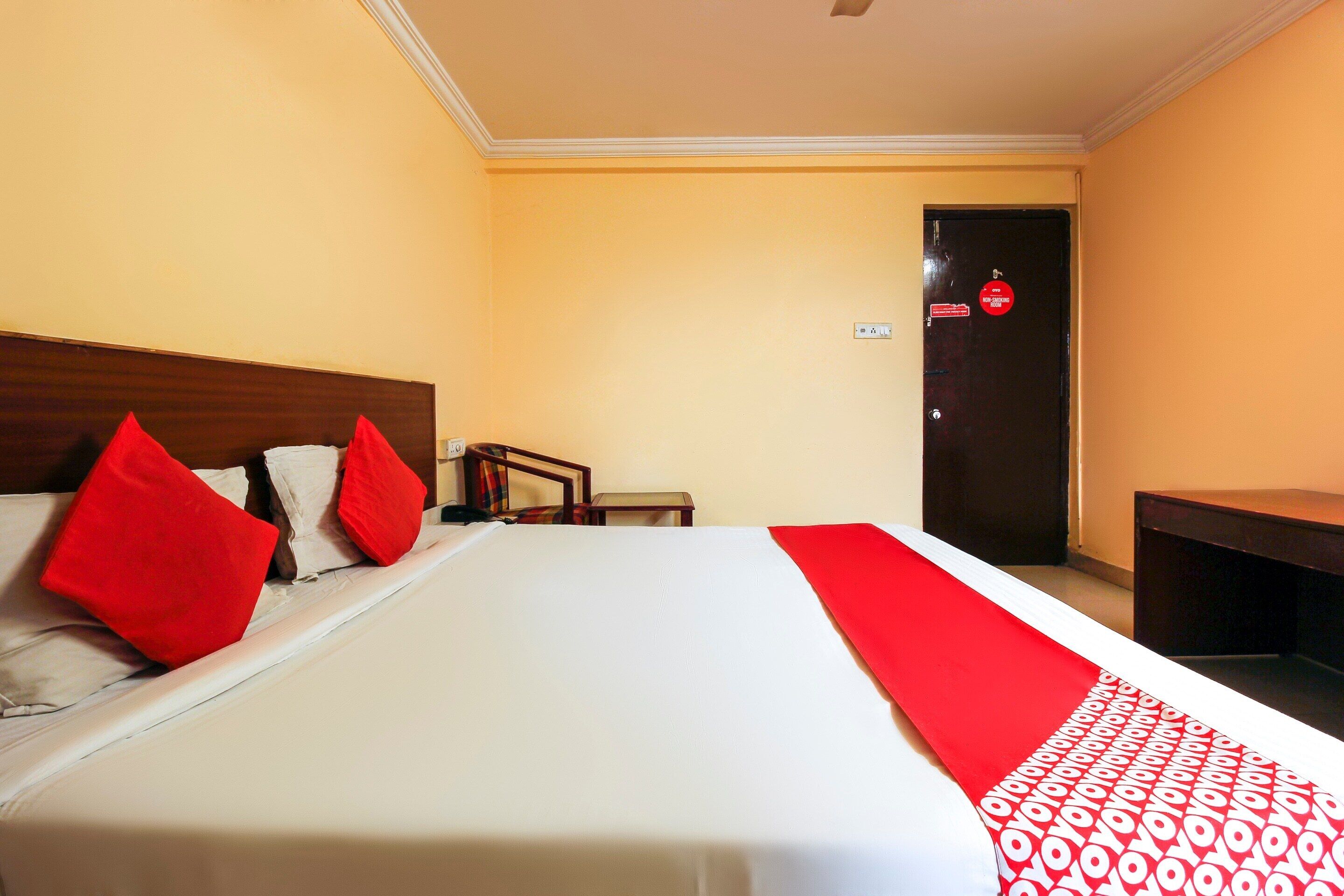 A hotel room with a bed, pillows, a bedside table, a chair, and a door with a non-smoking sign.