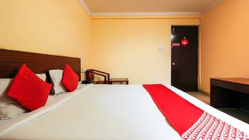 A hotel room with a bed, pillows, a bedside table, a chair, and a door with a non-smoking sign.
