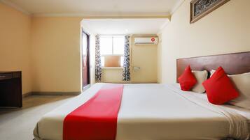A hotel room with a large bed, a wooden headboard, and a red accent pillow.
