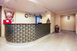 Un espace d’accueil avec un mur orné de motifs, un comptoir rouge, un ventilateur et un vase décoratif.