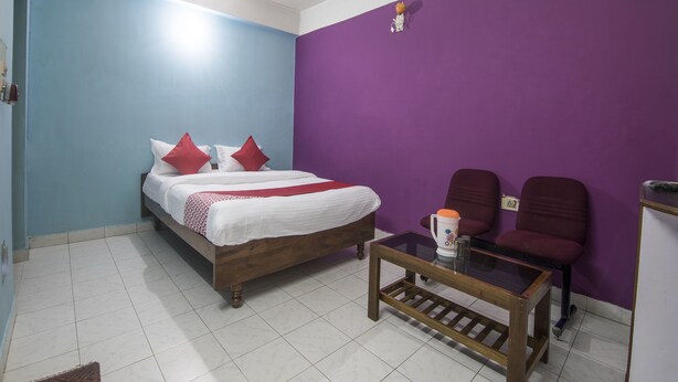 Een kamer met een bed, twee stoelen, een klein tafeltje en een paarse wand.
