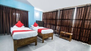 A hotel room with two wooden beds, red pillows, a wooden nightstand, a chair, and a large window with curtains. - OYO 14737 LG Towers (Guwahati)