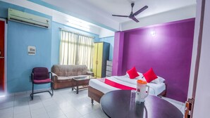 A hotel room with a bed, a sofa, a table, and a ceiling fan. - OYO 14737 LG Towers (Guwahati)