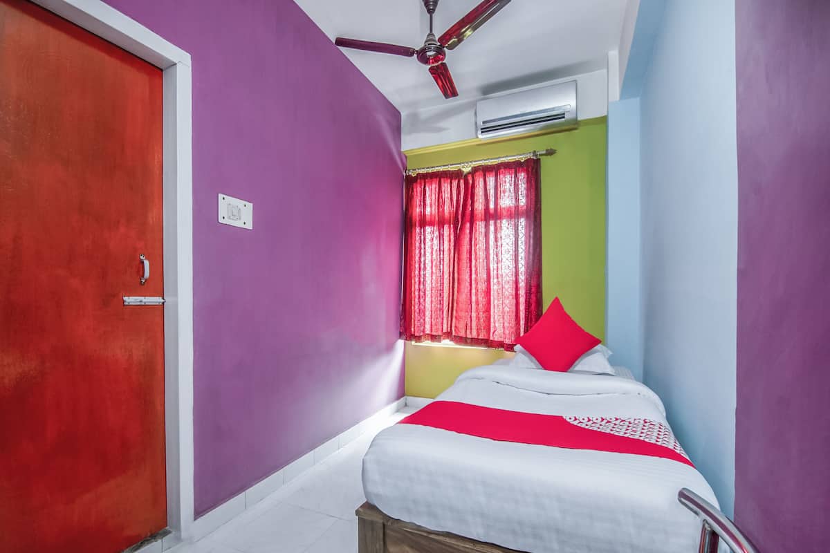 Een slaapkamer met een bed, een plafondventilator, een airconditioning en een raam met rode gordijnen.