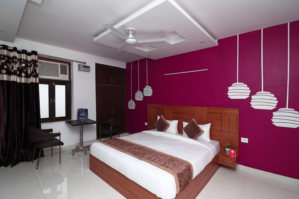 A bedroom with a large bed, a desk, a chair, a ceiling fan, and a window with curtains.