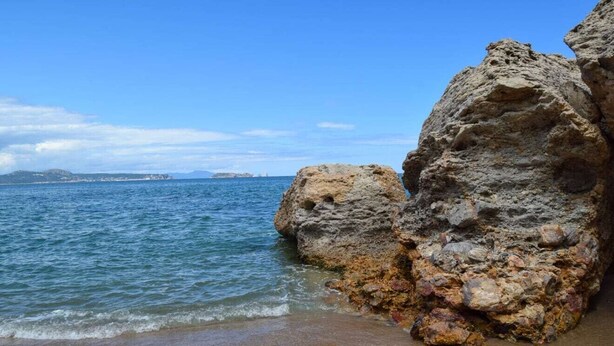 Une côte rocheuse bordée d’une eau d’un bleu limpide et s’étendant jusqu’à une terre lointaine.
