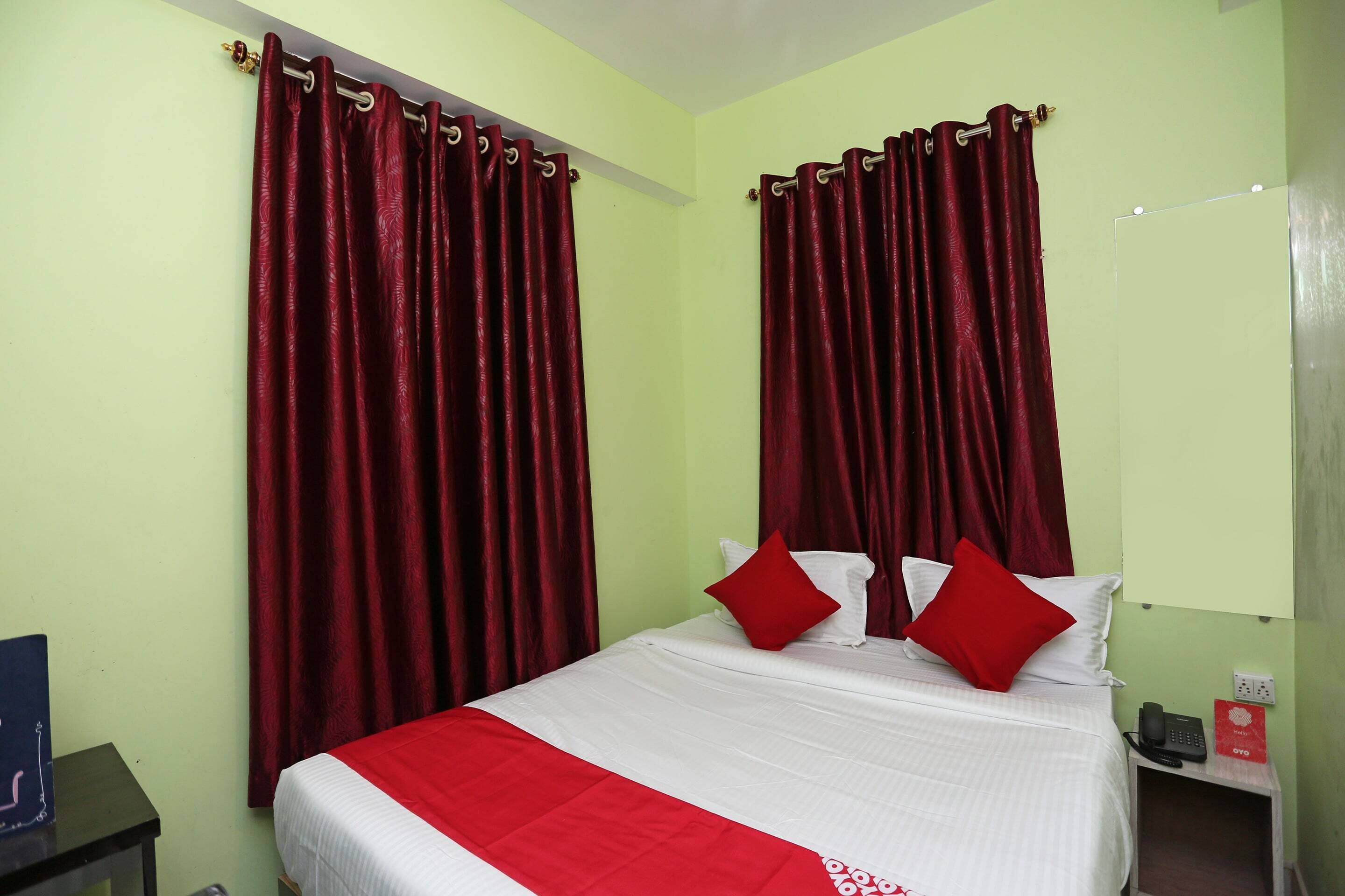 Una habitación de hotel con una cama, cortinas rojas, una colcha blanca y un plaid rojo.