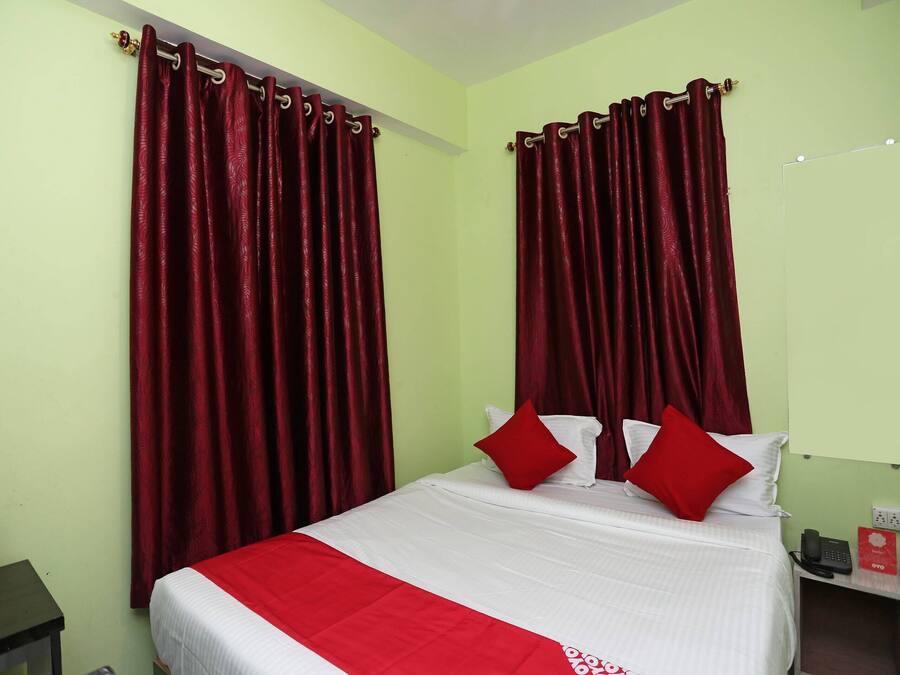 Una habitación de hotel con una cama, cortinas rojas, una colcha blanca y un plaid rojo.