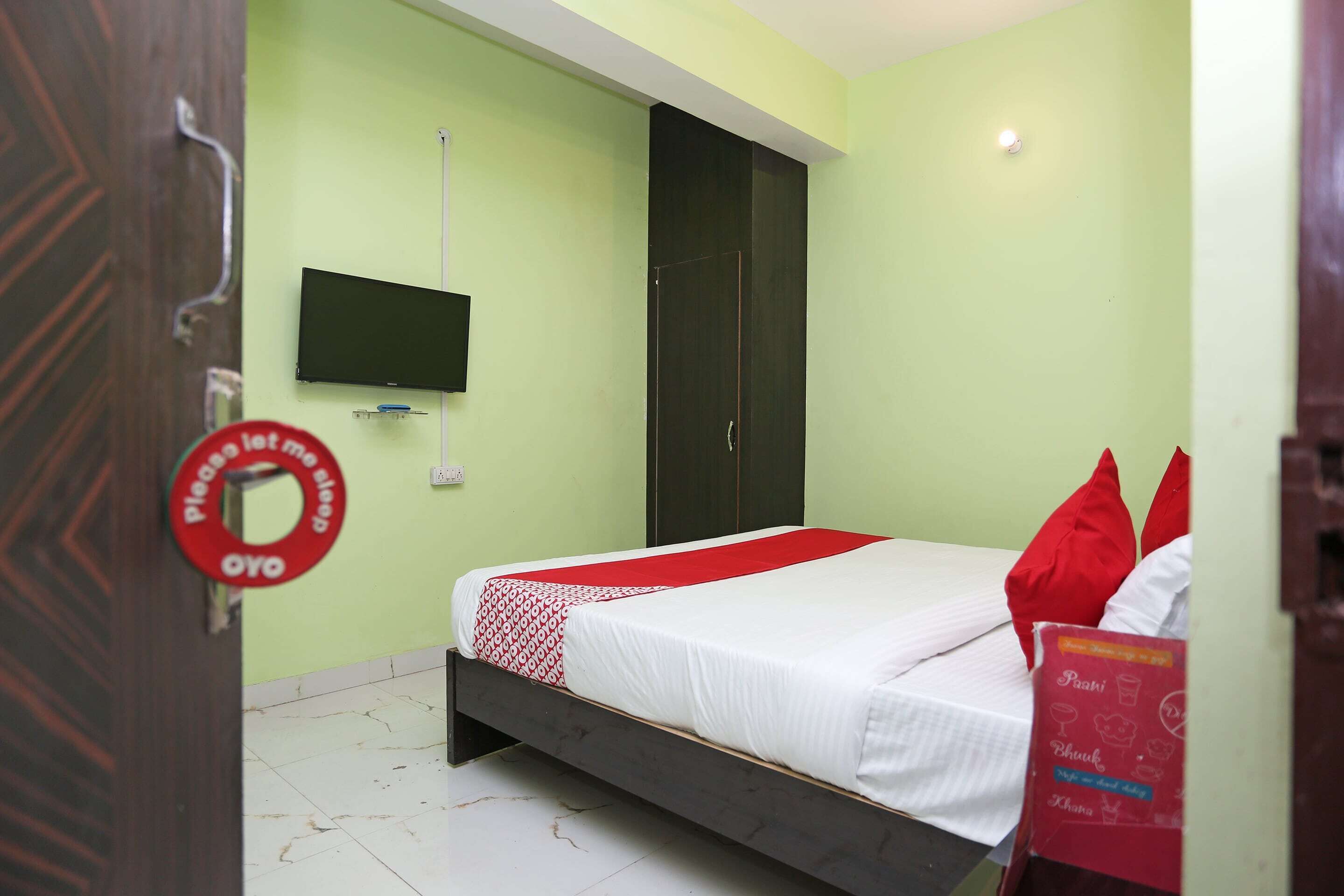 Een kamer met een bed, een aan de muur bevestigde televisie en een deur met een bordje.