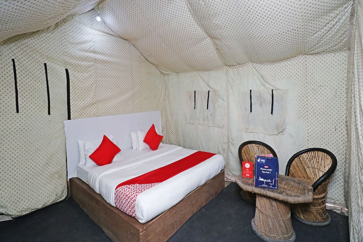A tent-style room with a bed, pillows, a small table, and two wicker chairs.