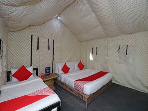 A tent-style room with two beds, each with red and white bedding, and a small table with a box of tissues.