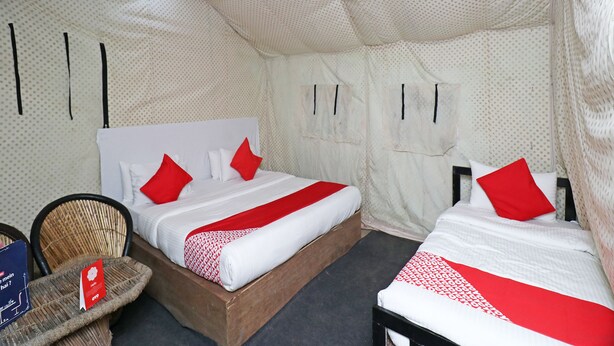A tent-style room with two beds, each with red and white bedding, and a small wicker chair with a sign. - OYO 26673 The Royal Rishikesh - Campsite (Rishikesh)