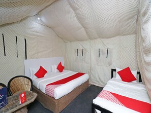A tent-style room with two beds, each with red and white bedding, and a small wicker chair with a sign.