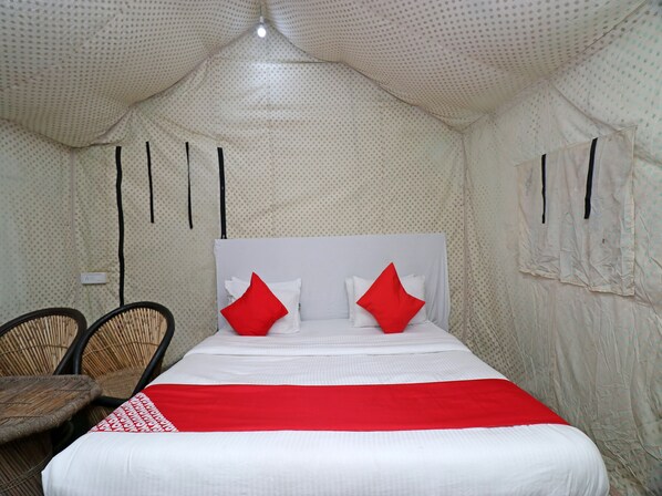 A bed with white bedding and red pillows, a red blanket, and a headboard. There are two wicker chairs and a small table. The room has a patterned ceiling and walls.
