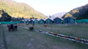 A row of tents in a grassy field with mountains in the background. - OYO 26673 The Royal Rishikesh - Campsite (Rishikesh)