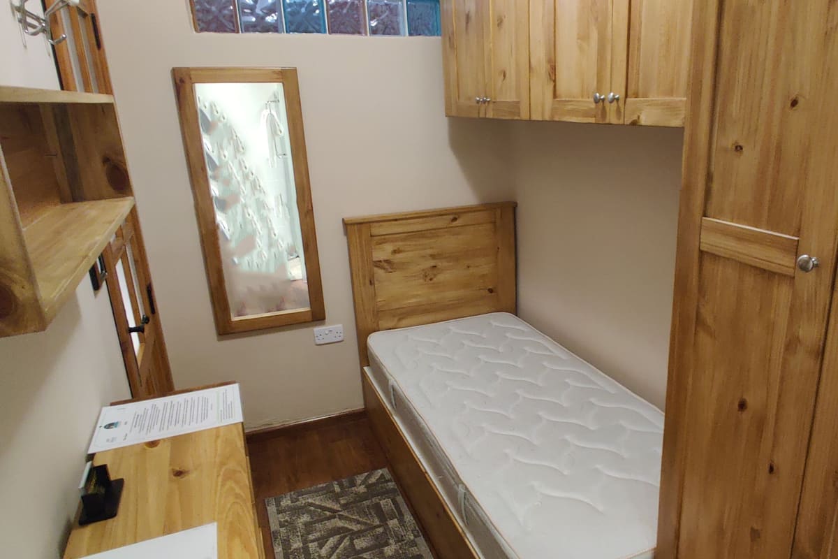 A small, compact room with wooden furniture, including a bed, a wooden cabinet, and a mirror.